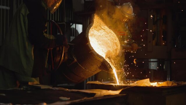 Industrial foundry workers pouring molten metal from a large ladle