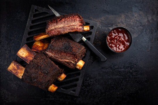 Traditional barbecue burnt chuck beef ribs marinated with spicy rub and served as top view on a rustic cast iron grillage