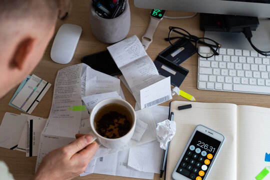 man holds cup in messy workplace with tickets, utility bills, receipts