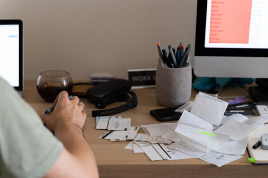 man works online at messy workplace with receipts, invoices