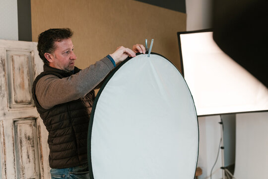 Focused male photographer mounting circular light reflector in studio