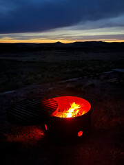 Sunsetting behind distant hills with a campfire pit glowing in the foreground. With steel blue...