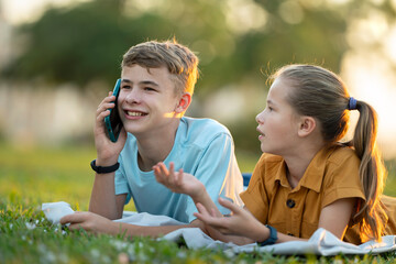 Happy young boy chatting on mobile phone ignoring his bored friend. Teenager friends having hard time communicating with each other. Friendship problems concept