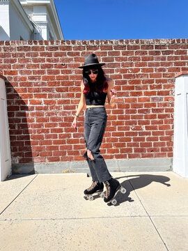Woman Roller Skating in Black Hat & Ripped Jeans with Brick Wall