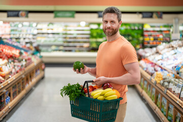 Handsome man with shopping basket with grocery. Man buying groceries in supermarket. Male model in...