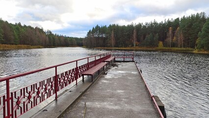 A pier with metal railings is built on the water near the lake shore. On the water ripples. There...