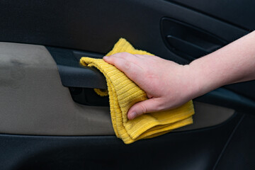 Close-up of a hand with a yellow microfiber cloth cleaning a car
