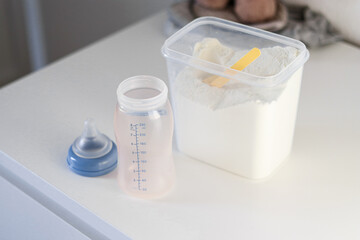 Dry powder formula milk for feeding babies in a can with yellow plastic scoop and empty feeding bottle