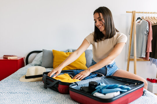 Young happy woman preparing suitcase for summer vacation trip. Travel and holidays concept.