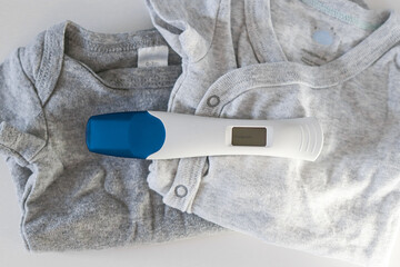 Close up of a digital positive pregnancy test on baby clothes