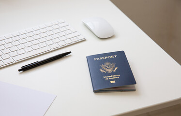 Close up of an American passport on white table, with a pan, a computer keyboard and mouse