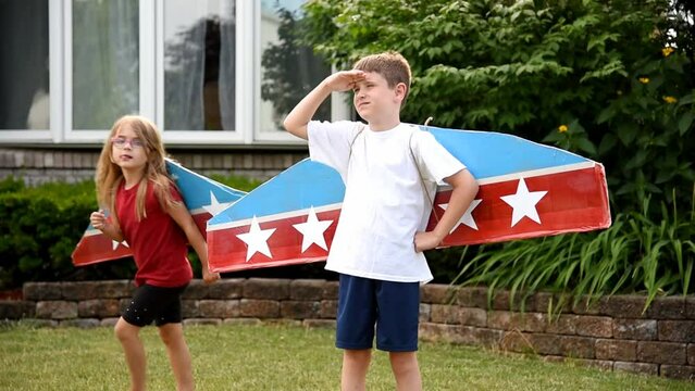 Children are wearing homemade cardboard flying wings with stars on them pretending to be a pilot outside for a craft, imagination or exploration concept.
