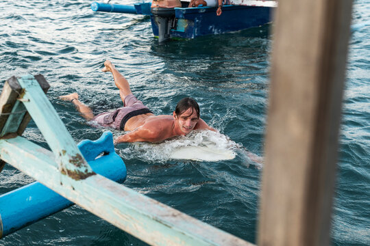 Surfer with a surfboard getting ready to catch waves close to a boat