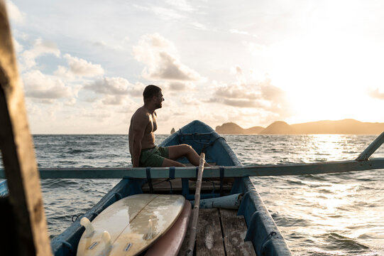 Exhausted surfer on boat next to surfboards