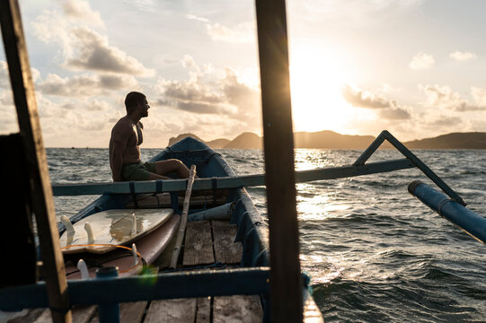 Surfer on boat next to surfboards at summertime