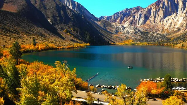 Aerial Shot Of Nautical Vessel In Lake Amidst Mountains, Drone Ascending Backwards Over Trees On Sunny Day - Mammoth Lakes, California
