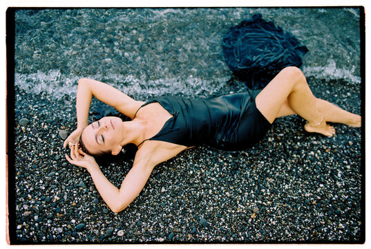 Film photo of woman in a cocktail dress lying at the seashore