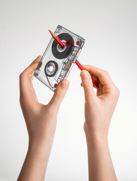 Hands winding cassette tape with red pencil. Nostalgia for childhood