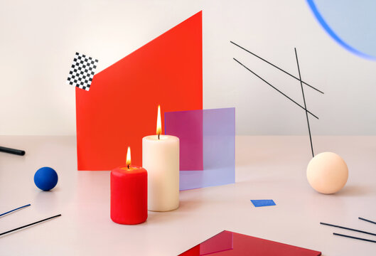 Two burning candles on a beige background with geometric elements.