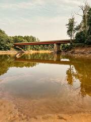Fototapeta premium Rural Scene of a Bridge Overpass Over a River. A bridge overpass on the Sangamon River in Petersburg, Illinois. Low water levels due to drought conditions. Leafy green trees surround the scene.