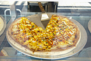 A freshly baked specialty pizza placed behind glass, to be sold by the slice from a small store...
