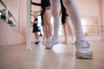 Fototapeta na wymiar Little girls practice ballet at the barre. Close-up of young ballerinas' feet. 