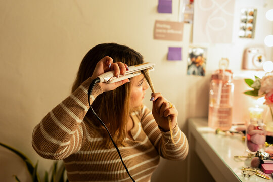teen woman straightening her hair with a straightener