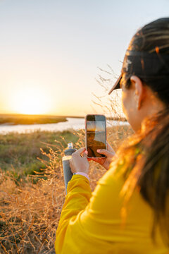 Sporty woman taking cellphone picture of sunset