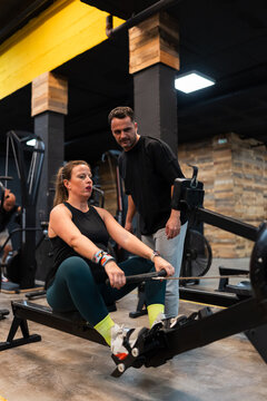 pregnant woman rowing in the gym under the watchful eye of her trainer