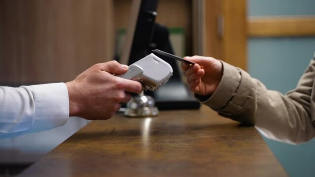 Woman making payment with credit card, receptionist holding credit card reader in hotel