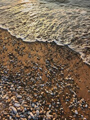 Tranquil scene of small pebbles and golden sand on the peaceful beach with gentle waves under the warm sunlight, perfect for relaxation and mindfulness, nature background for meditation and serenity