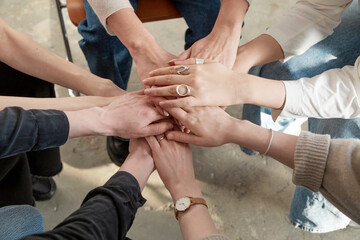 Crop people stacking hands while sitting on chairs