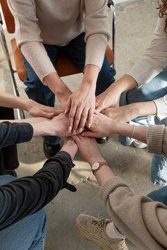 Crop people stacking hands together while sitting on chairs