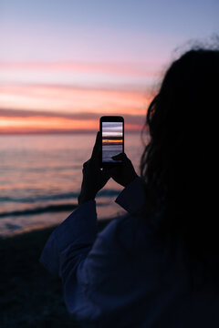A Woman On the Beach Photographing the Sunset