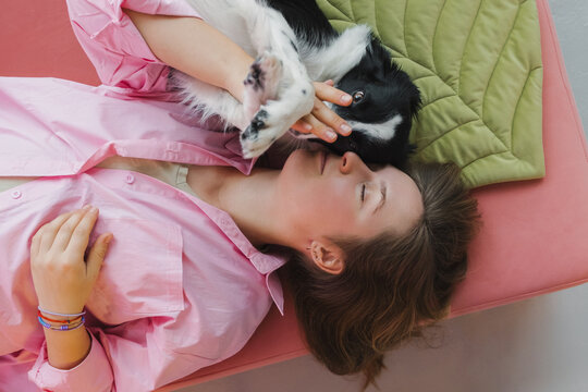 Happy woman with adorable dog lying on pink floor
