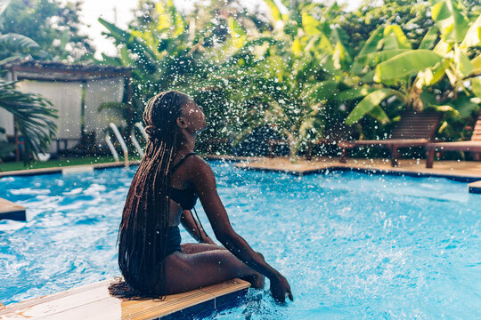 Young woman sitting by edge of swimming pool and splashing water