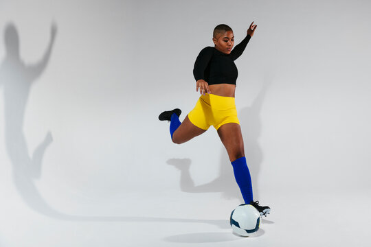 Portrait of woman kicking ball in studio