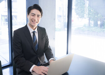 Asian (Japanese) businessman looking at the camera while working on his laptop
