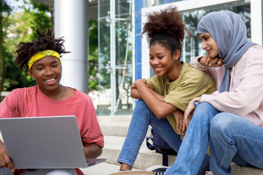 Happy diverse friends studying on laptop in campus