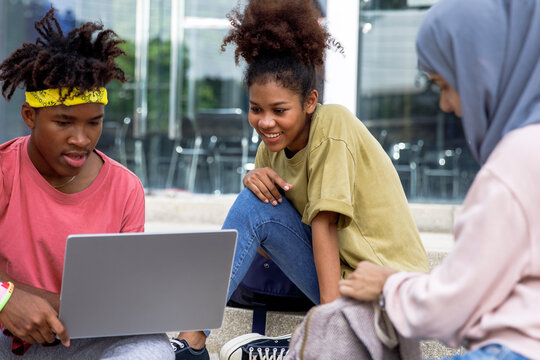 Happy multiracial friends studying on laptop in university