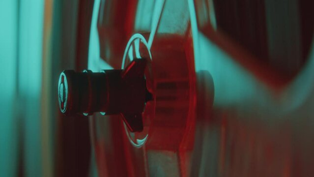 Reel spindle turning while playing music with retro reel-to-reel tape recorder in dark studio with colorful neon light. Close up view