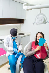 A female dentist puts on medical gloves and patient checking denture in a mirror in a dental office. Happy patient and dentist concept.