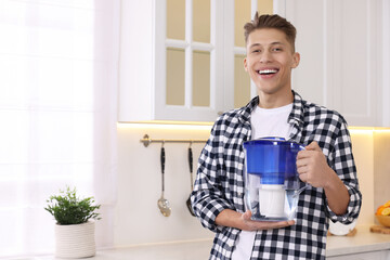 Happy man with water filter jug in kitchen. Space for text