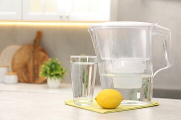 Water filter jug, glass and lemon on light grey table in kitchen, space for text