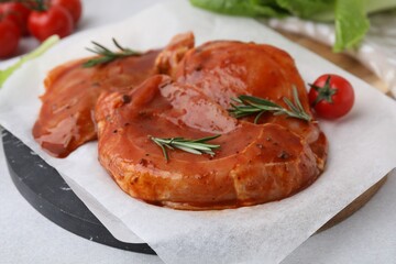 Board with raw marinated meat and rosemary on light table, closeup