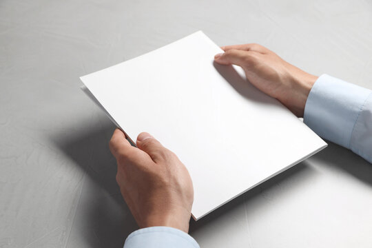 Man holding blank notebook at light grey table, closeup. Mockup for design