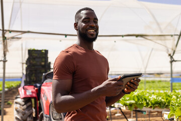 African American young male farm supervisor holding a tablet, standing in a greenhouse at a hydropon
