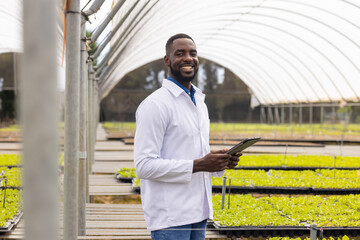 African American young male farm supervisor holding a tablet, standing in a greenhouse