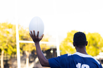 African American young male athlete, holding a rugby ball, ready to throw, copy space