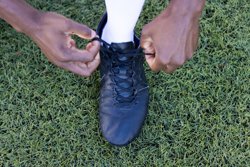 African American young male athlete tying black shoe laces on a grass field outdoors